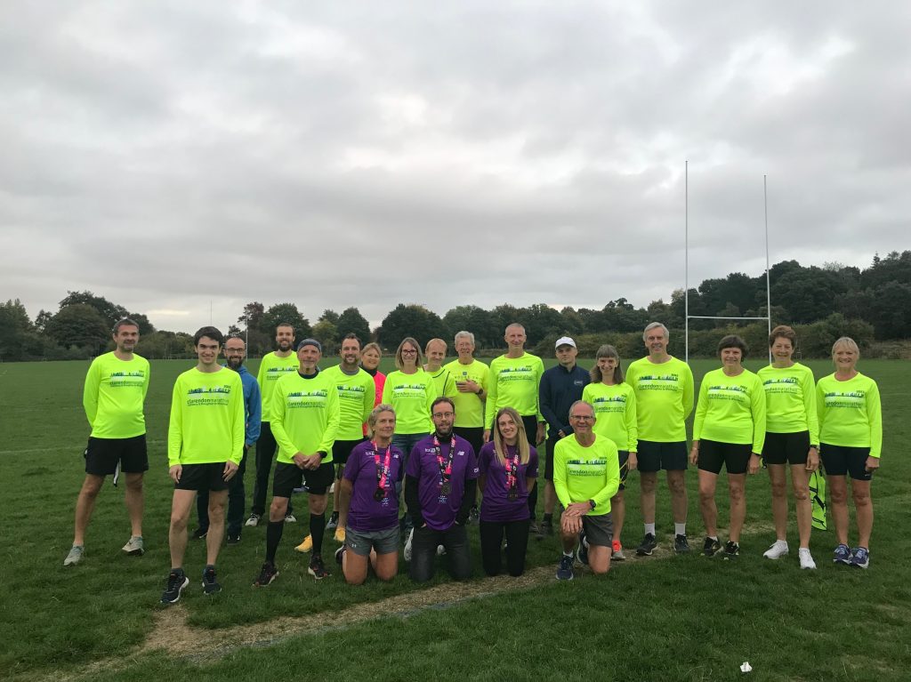 21 runners mostly in yellow clarendon shirts with 3 in purple london shirts standing in a field 