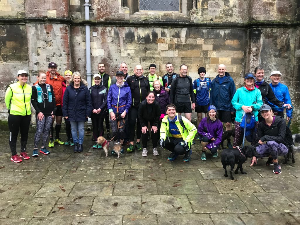 A group of wet runners and a couple of dogs outside an abbey