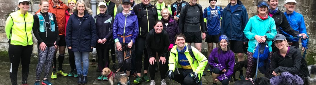 A group of wet runners and a couple of dogs outside an abbey