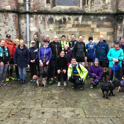A group of wet runners and a couple of dogs outside an abbey